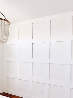 a room with white walls and wood flooring in the corner is furnished with a chandelier