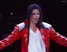 a man in red and white jacket on stage with his hands out to the side