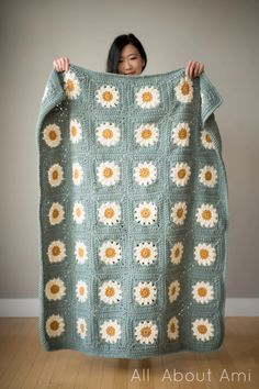 a woman holding up a crocheted blanket with sunflowers on it