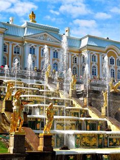 an elaborate fountain in front of a large building with gold statues on it's sides