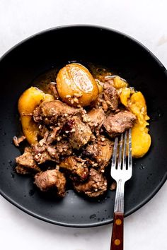 meat and potatoes in a black bowl with a fork