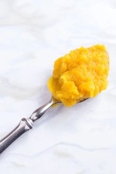 a spoon filled with yellow food on top of a white countertop next to a knife