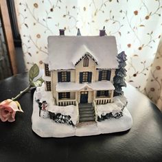 a doll house sitting on top of a table next to a pink rose and curtain