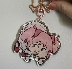 a hand holding a pink and white keychain with an anime character on it