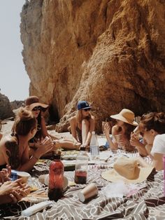 a group of people sitting on top of a beach next to each other near a cliff