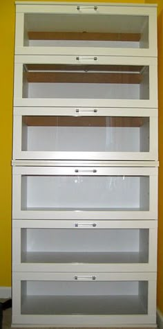 a tall white shelf with glass doors on the top and bottom, in front of a yellow wall