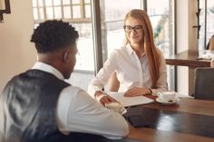 a woman sitting at a table in front of a man who is talking to her