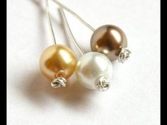 three different colored pearls are hanging from silver hooks on a white surface, one is gold and the other is silver