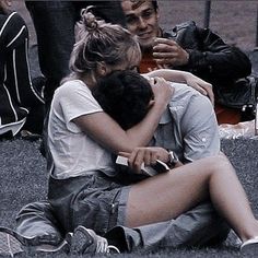 two people sitting on the ground with their arms around each other and one person covering his face