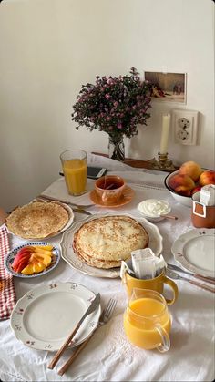 the table is set for breakfast with fruit and bread on it, along with orange juice