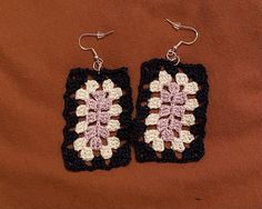 two crocheted square shaped earrings on top of a brown cloth with silver hooks