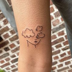 a woman's arm with a small tattoo of a head and clouds on it