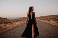 a woman in a black dress is walking down the road with her leg slit open