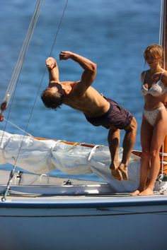 a man and woman standing on the deck of a sailboat while another person watches