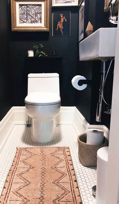 a white toilet sitting in a bathroom next to a rug on the floor and framed pictures above it