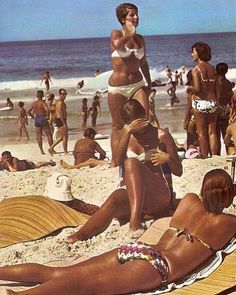 several people are on the beach in bathing suits and bikinis, while one person is holding a cell phone up to her ear