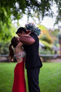 a man and woman kissing under a tree with an american football on their foreheads