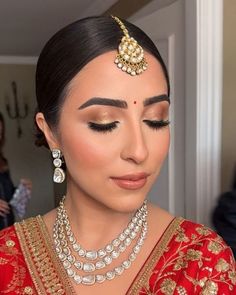 a woman wearing a red and gold bridal outfit with jewelry on her head, looking down at the camera