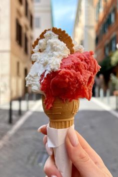 someone is holding an ice cream cone with red and white toppings in the street