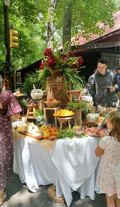 a group of people standing around a table with food on it and flowers in vases