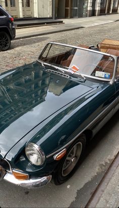 an old green convertible car parked on the side of the road next to a building