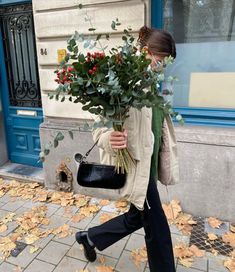 a woman walking down the street with a bouquet of flowers in her hand and wearing a face mask