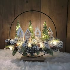 a christmas centerpiece with small houses and pine trees in the center surrounded by white lights