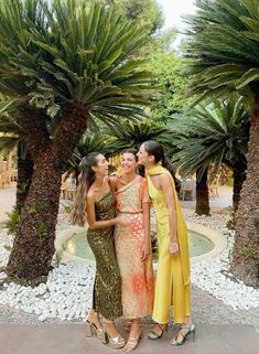 three women standing next to each other in front of palm trees