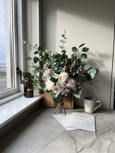 a bouquet of flowers sitting on top of a counter next to a cup and book