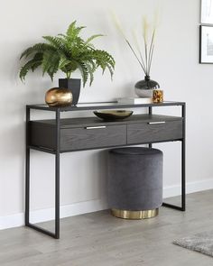 a black and gold console table with two plants on it, next to a grey stool