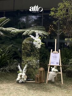 an easel with white flowers and greenery is set up for a wedding ceremony