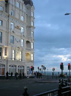 people are standing on the sidewalk in front of a large white building with many windows