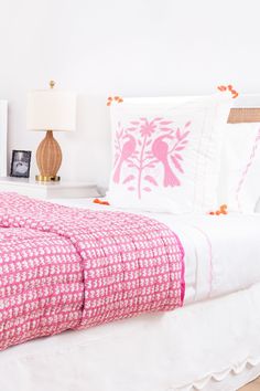 a white bed topped with pink and white pillows next to a nightstand filled with pictures