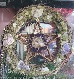 a wreath hanging from the side of a building with moss and rocks around it in front of a window