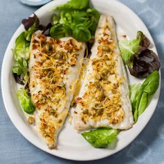 two fish on a plate with lettuce and olives