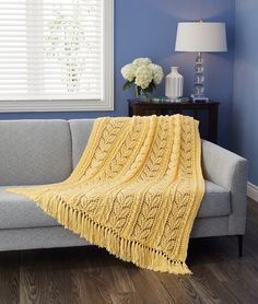 a couch with a yellow blanket on top of it next to a lamp and window