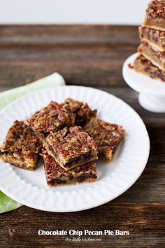 chocolate chip pecan pie bars on a white plate next to a stack of brownies