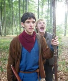 two young men standing in the woods with their arms around each other and one holding a stick