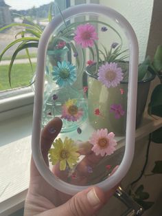 a person holding up a mirror with flowers in it