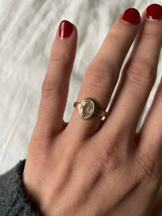 a woman's hand wearing a gold ring with a white diamond on it and red nail polish