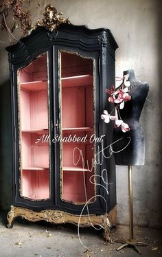 an old china cabinet is painted black with gold trim and pink glass doors, along with a mannequin's dummy