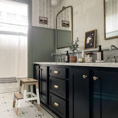 a bathroom with black cabinets and white tile flooring, two framed pictures on the wall