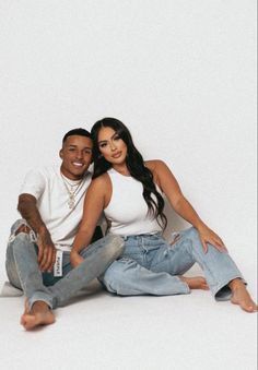 a man and woman are sitting on the floor posing for a photo in front of a white background