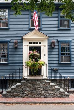 a blue house with an american flag on the front door and flowers in potted planters