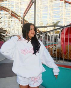 a woman in white sweatshirt and shorts standing next to roller coaster