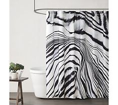 a zebra print shower curtain hanging on a wall next to a bathtub and toilet