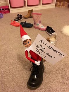 an elf is holding a sign in front of some shoes on the floor, and there are