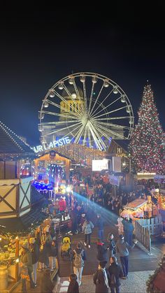 people are walking around in front of a christmas tree and ferris wheel at the fair