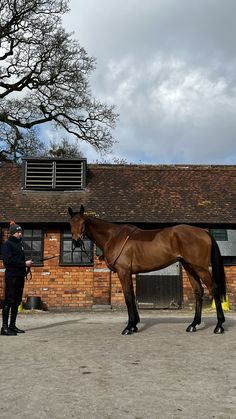 a man standing next to a brown horse in front of a brick building with a black roof