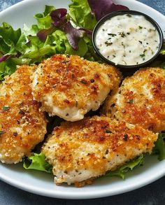 a white plate topped with chicken cutlets next to a salad and dipping sauce on top of it